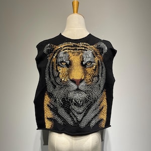 May include: Black sleeveless shirt with a tiger face design made of gold and silver safety pins.