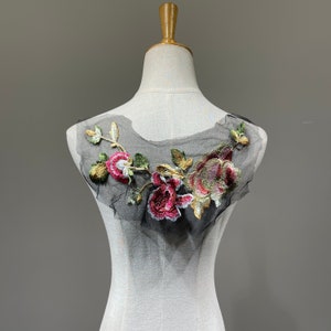 Könnte beinhalten: Eine schwarze Mesh-Applikation mit gestickten rosa, goldenen und grünen Blumen. Die Applikation ist perfekt, um Kleidung oder Bastelarbeiten einen Hauch von Eleganz zu verleihen.