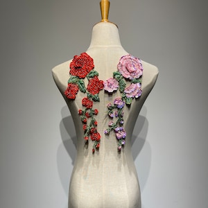 May include: A pair of floral appliques featuring red, pink and purple flowers with green leaves. The appliques are displayed against a white background.