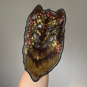 May include: A gold, brown and silver sequined wolf head applique with a black mesh backing.