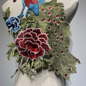 May include: Embroidered floral applique featuring a peacock and peony design. The peacock has blue and red details, while the peony is a deep red with white accents. Green leaves and a blue flower complete the design.