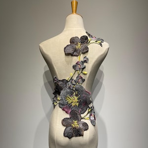 Puede incluir: Una aplicación floral negra y verde con un diseño de vid. La aplicación está hecha de tela y tiene un efecto 3D.