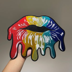 Puede incluir: Parche de hierro bordado de color arcoíris de una boca abierta que gotea, se derrite y tiene un contorno negro.