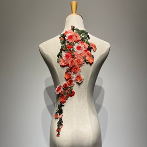 May include: A delicate floral applique featuring a cascade of pink and orange flowers with green leaves. The applique is perfect for adding a touch of elegance to clothing, accessories, or home decor projects.