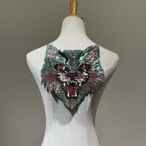 Op de afbeelding: Groene en roze pailletten applicatie van een kattenkop met zwarte ogen en een open rode mond.