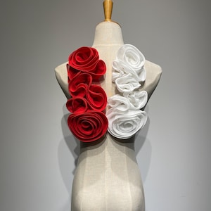 May include: A white and red fabric flower embellishment on a dress form. The flowers are made of multiple layers of fabric and are arranged in a circular pattern.