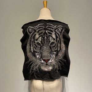 Puede incluir: Top negro sin mangas con un rostro de tigre blanco bordado en la espalda. El rostro del tigre está hecho de lentejuelas y cuentas plateadas.