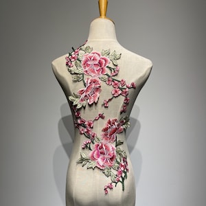Può includere: Applicazione floreale ricamata con grandi fiori di peonia rosa e fiori rosa più piccoli con foglie verdi. Il design è applicato a un manichino, mostrando gli intricati dettagli del motivo floreale. Ideale per abbellire capi di abbigliamento o progetti artigianali.
