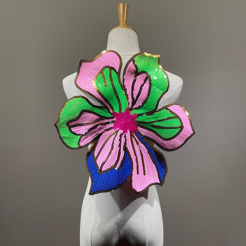 May include: A large, pink, green, and blue sequined flower applique. The flower has a gold outline and is perfect for adding a touch of sparkle to any project.