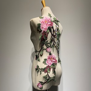 Pode incluir: Uma aplica&ccedil;&atilde;o floral rosa e verde com p&aacute;ssaros sobre um fundo branco. A aplica&ccedil;&atilde;o &eacute; feita de tecido bordado e &eacute; perfeita para adicionar um toque de eleg&acirc;ncia a qualquer projeto.