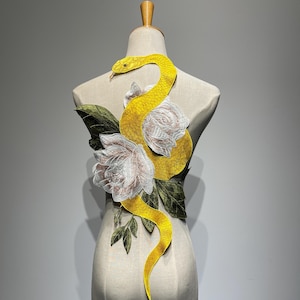 May include: A yellow embroidered snake design with a textured pattern, winding around two white and pink roses and green leaves. The design is displayed on a mannequin, showcasing the potential for apparel embellishment.