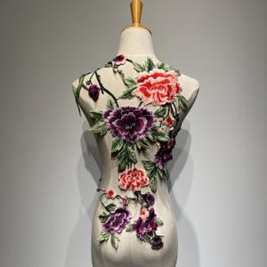 May include: A floral applique with pink, red, and purple flowers and green leaves. The applique is on a white background.