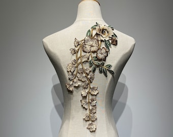 May include: A delicate floral applique with brown and green embroidery. The design features a large flower at the top with smaller flowers cascading down the stem.