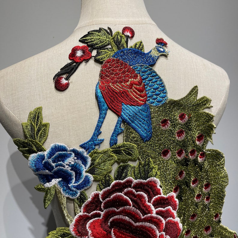 May include: Embroidered peacock patch with a vibrant design. The peacock features red, blue, and green thread, surrounded by detailed floral elements in red, blue, and green. The patch is designed for fabric embellishment.