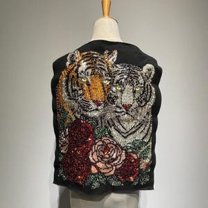 May include: Black sleeveless vest with a beaded design of two tigers, one orange and black and the other white, with red and green roses.