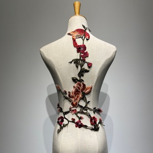 May include: A brown fabric mannequin with a floral applique design. The applique features red and green flowers, leaves, and a small bird.