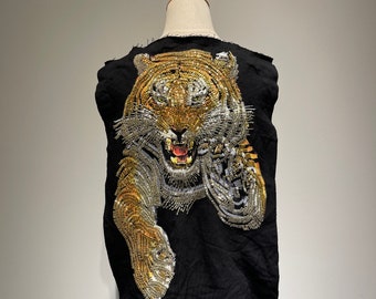 May include: A black sleeveless vest with a tiger design made of gold and silver embellishments. The tiger is facing forward with its mouth open and its teeth showing.