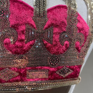 May include: A close-up of a red velvet crown with gold sequin embellishments. The crown has a pointed top and a rounded base.