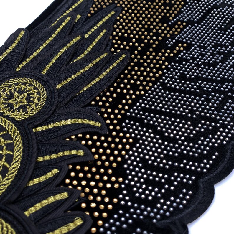 May include: Black fabric with gold and silver embellishments. The fabric has a pattern of small circles and a design of wings with a circular emblem.