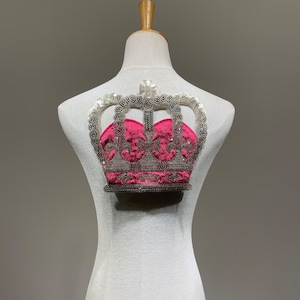 Può includere: Una corona argentata e rosa con paillettes e perline su un manichino bianco.
