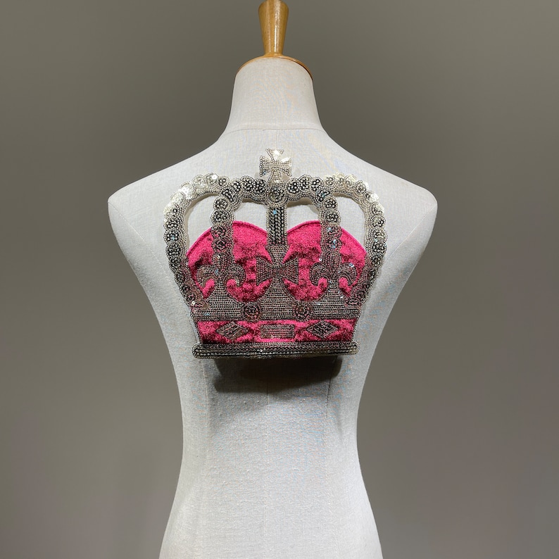 May include: A silver and pink crown with sequins and beads on a white mannequin.
