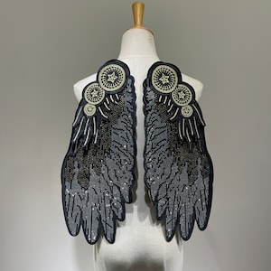 Puede incluir: Un par de alas negras con adornos dorados. Las alas están hechas de tela y tienen un acabado brillante. Son perfectas para agregar un toque de drama a cualquier atuendo.