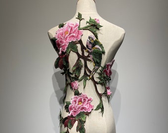 May include: A pink and green floral applique with two birds perched on a branch. The applique is embroidered with delicate details and would be perfect for adding a touch of elegance to a garment or craft project.