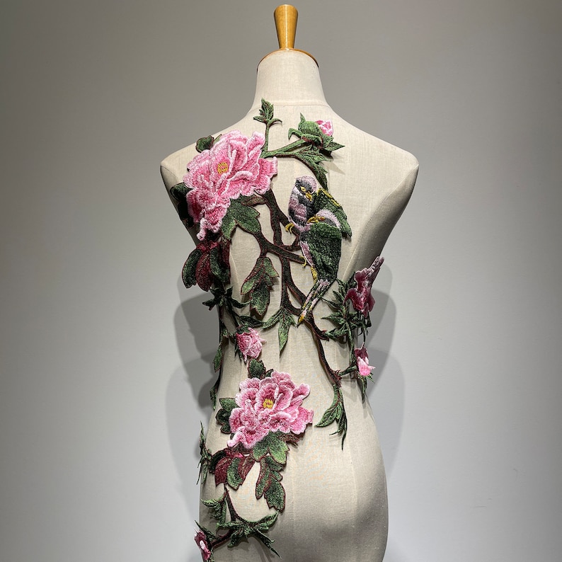 Pode incluir: Uma aplica&ccedil;&atilde;o floral rosa e verde com dois p&aacute;ssaros empoleirados em um galho. A aplica&ccedil;&atilde;o &eacute; bordada com detalhes delicados e seria perfeita para adicionar um toque de eleg&acirc;ncia a uma roupa ou projeto artesanal.
