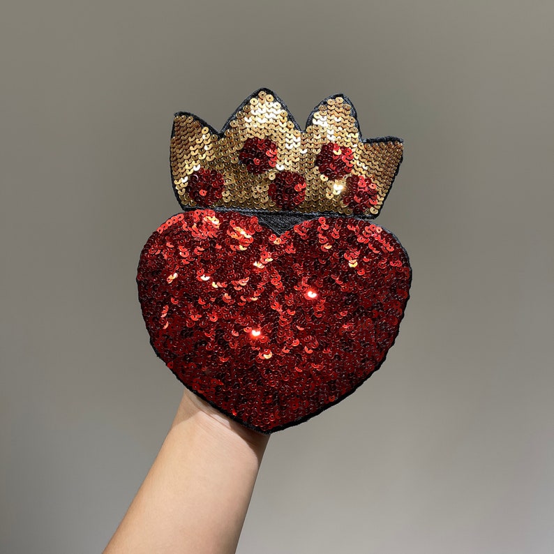 K&ouml;nnte beinhalten: Ein roter herzf&ouml;rmiger Patch mit goldenen Pailletten und einem Kronendesign. Der Patch besteht aus Stoff und Pailletten und ist perfekt, um jedem Projekt einen Hauch von Glanz zu verleihen.
