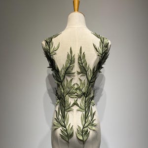 Peut inclure: Broderie de motif floral vert feuillu sur un tissu transparent. Le motif est en forme de vigne avec des feuilles et des branches.