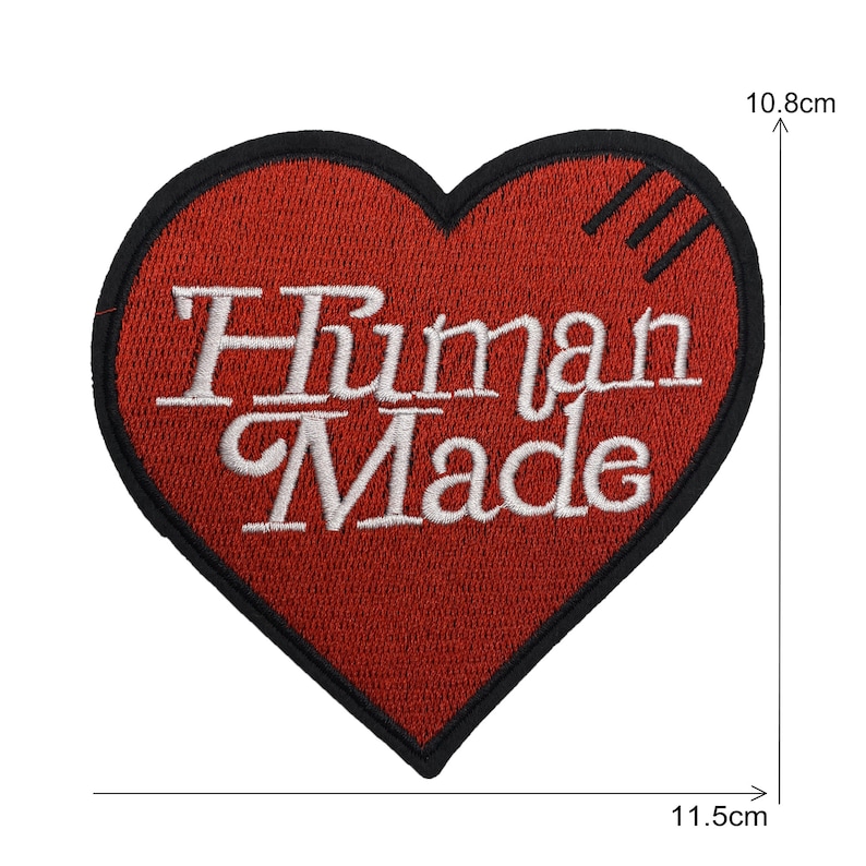 May include: Red heart-shaped embroidered patch with black outline and white text that reads "Human Made". The patch measures 10.8 cm by 11.5 cm.