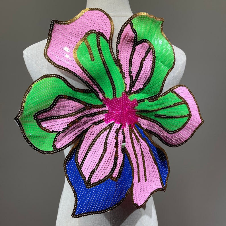 May include: A large pink, green, and blue sequined flower applique. The flower has a gold outline and a pink center.