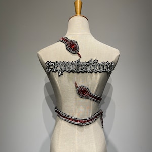 Può includere: Un manichino bianco con un design a serpente rosso e argento sul busto. Il design include la parola "reputation" in strass argentati.