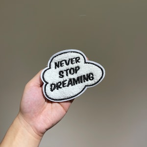 May include: White cloud-shaped patch with black embroidery that reads "Never Stop Dreaming".