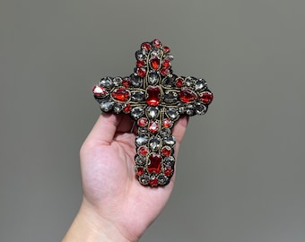 May include: A black cross with red and silver rhinestones. The cross is embellished with gold thread.
