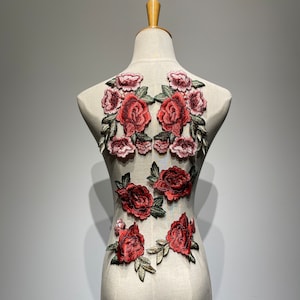 Può includere: Un set di applicazioni ricamate di rose rosse e rosa con foglie verdi. Le applicazioni sono disposte in modo simmetrico su uno sfondo bianco.