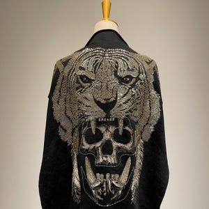 Puede incluir: Chaqueta negra con un diseño de tigre y calavera plateado bordado en la espalda.