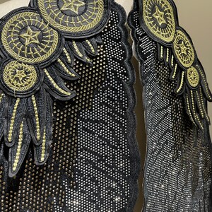 May include: Two black fabric patches with gold embroidery and rhinestones. The patches feature a wing design with a star and circle motif.