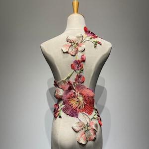 May include: A white dress form with a floral applique design. The applique is made of red, pink, and white fabric and features a variety of flower shapes.