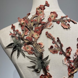 May include: A brown and green embroidered applique featuring a floral design with delicate branches and leaves. The applique is perfect for adding a touch of elegance to clothing, accessories, or home decor projects.