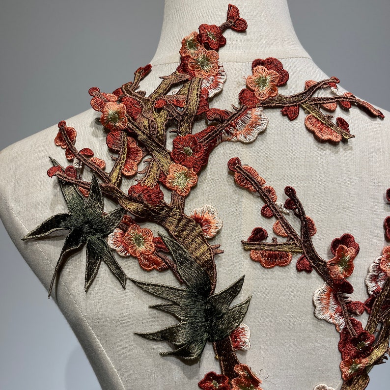 May include: A brown and green embroidered applique featuring a floral design with delicate branches and leaves. The applique is perfect for adding a touch of elegance to clothing, accessories, or home decor projects.