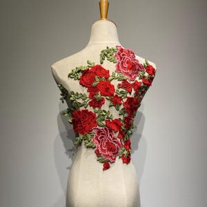 Peut inclure: Applique de broderie florale rouge et verte. L'applique présente un groupe de roses rouges avec des feuilles et des tiges vertes.