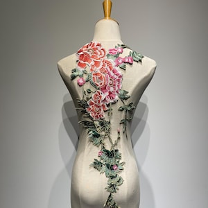 May include: A floral applique with pink and red flowers and green leaves. The applique is on a white background.