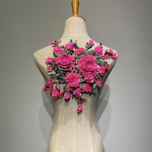 Peut inclure: Applique florale rose vif avec des motifs de fleurs détaillés et superposés et des feuilles vertes. L'applique est présentée sur un mannequin, ce qui suggère son utilisation dans des projets de mode ou d'artisanat. Le design est complexe et attrayant.