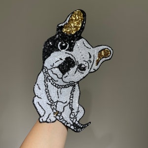 Könnte beinhalten: Ein weißer und schwarzer Französischer Bulldogge mit goldenen Glitzerakzenten, der eine silberne Kettenkette trägt. Der Bulldogge sitzt mit dem Kopf zur Seite geneigt und der Zunge herausgestreckt. Das Bild ist eine Nahaufnahme des Gesichts und Körpers des Bulldogs.