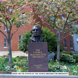 May include: A bronze bust of George Washington in front of a brick building with a sign that reads "The George Washington University Founded 1821". The bust is surrounded by pink flowering trees and green bushes.