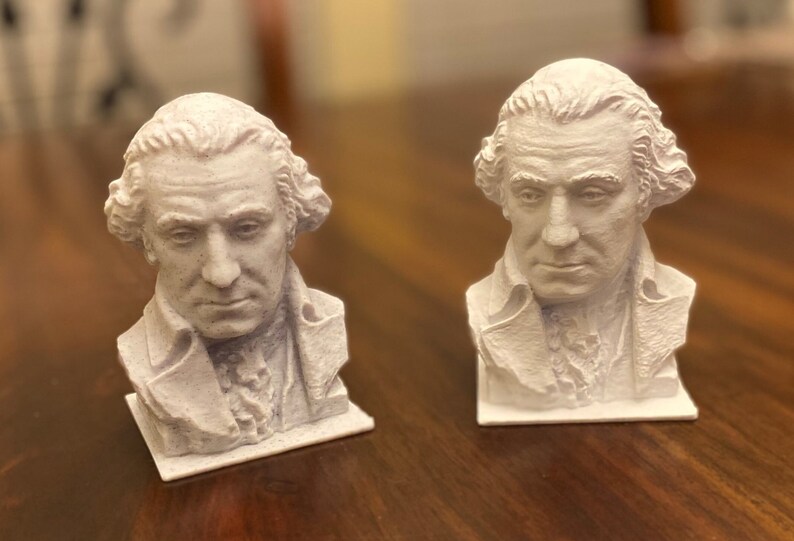 May include: Two white plaster busts of a man with a powdered wig. The busts are on small square bases.