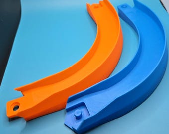 May include: Two curved toy track segments, one bright orange and one vibrant blue. Each piece features a raised side wall, a flat base, and a circular connector hole at one end with a corresponding peg on the other end for interlocking assembly.
