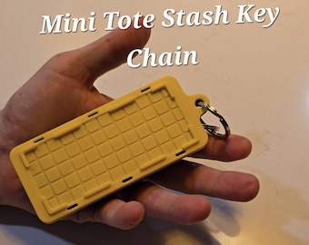 May include: Yellow Mini Tote Stash Key Chain. The rectangular keychain has a textured grid pattern and a metal keyring. The text "Mini Tote Stash Key Chain" is displayed in white.