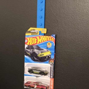 May include: A Hot Wheels toy car packaging featuring a black and green car with yellow accents. The packaging also includes a red car and the text "Hot Wheels Legends Tour Winner!" and "New for 2025".